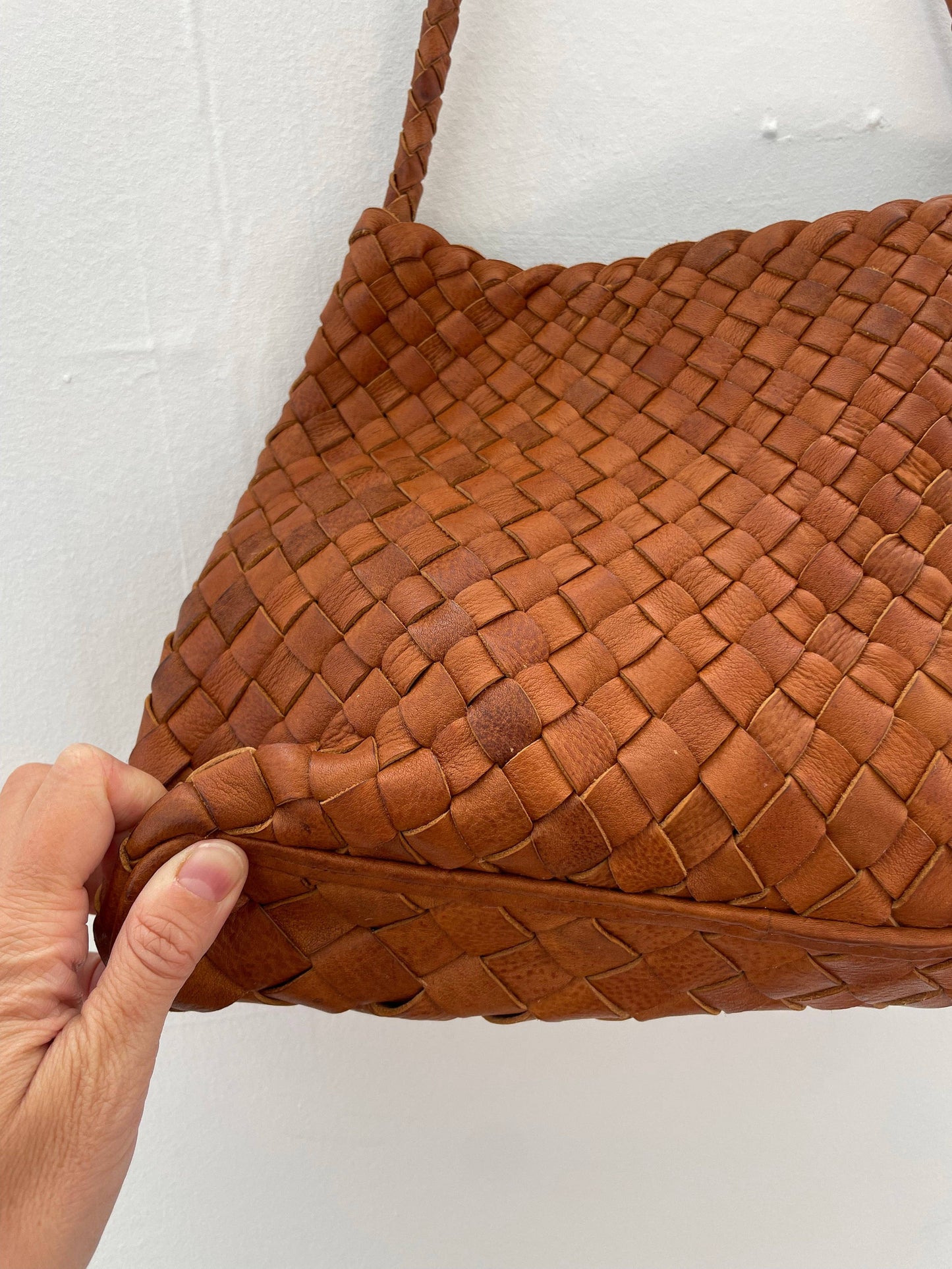 Close-up of a hand holding the Palar Tan Bag to show its woven leather texture