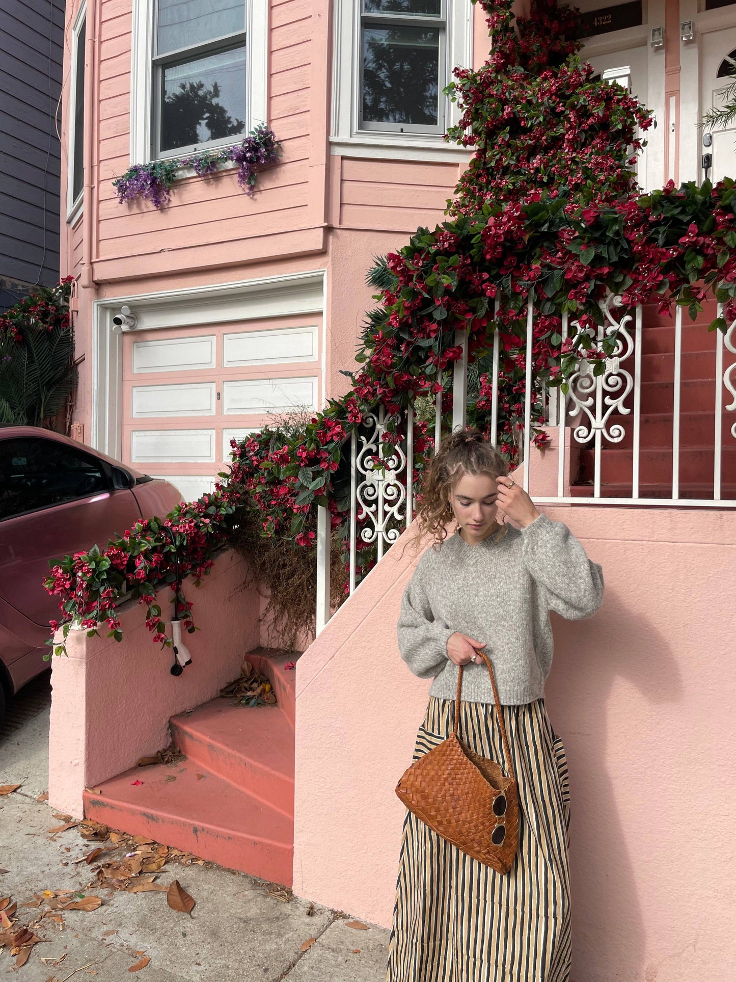 Model carrying the Palar Tan Bag outside a pink house with flowering vines