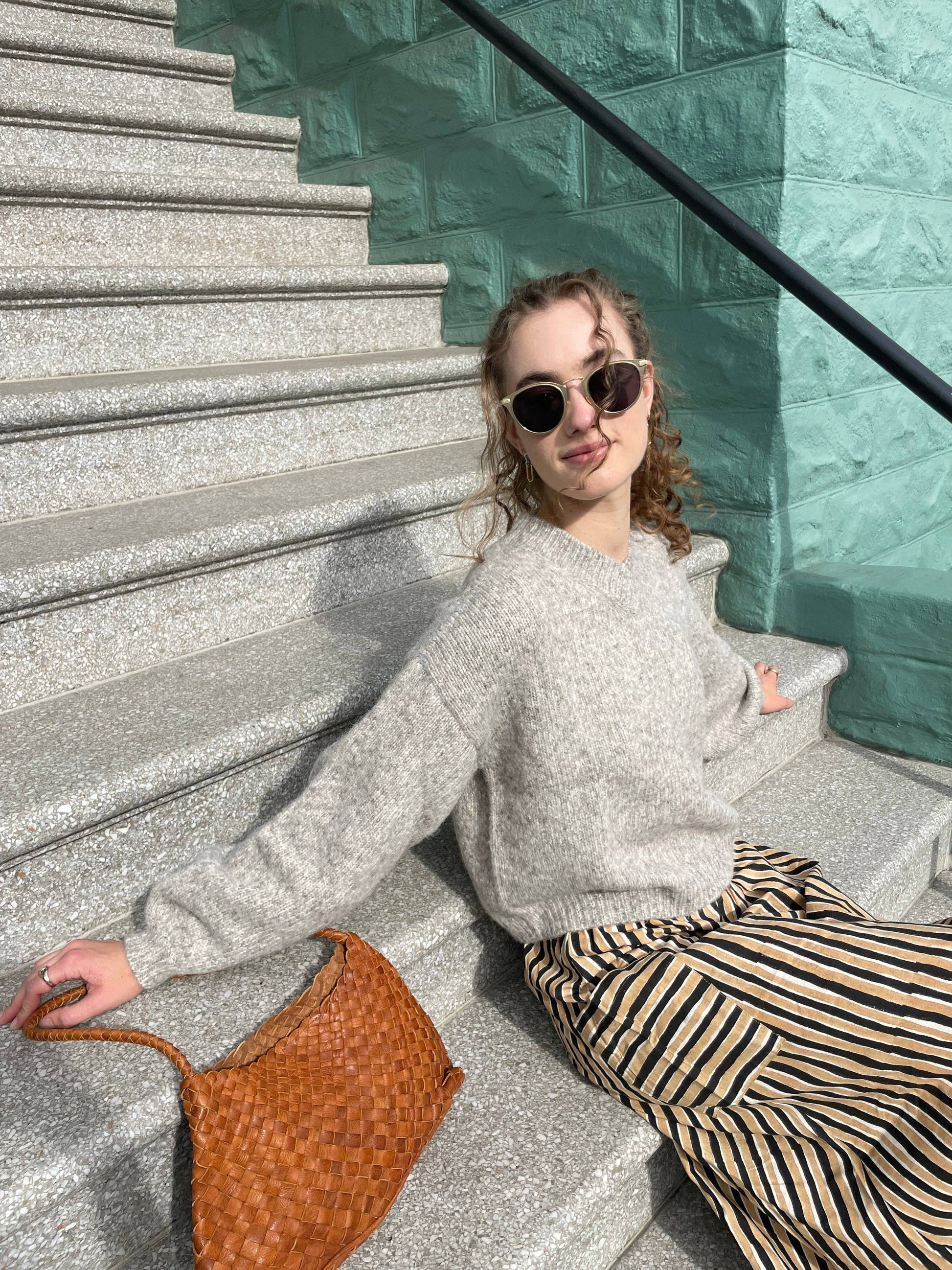 Model seated on steps beside the Palar Tan Bag in a relaxed street-style look