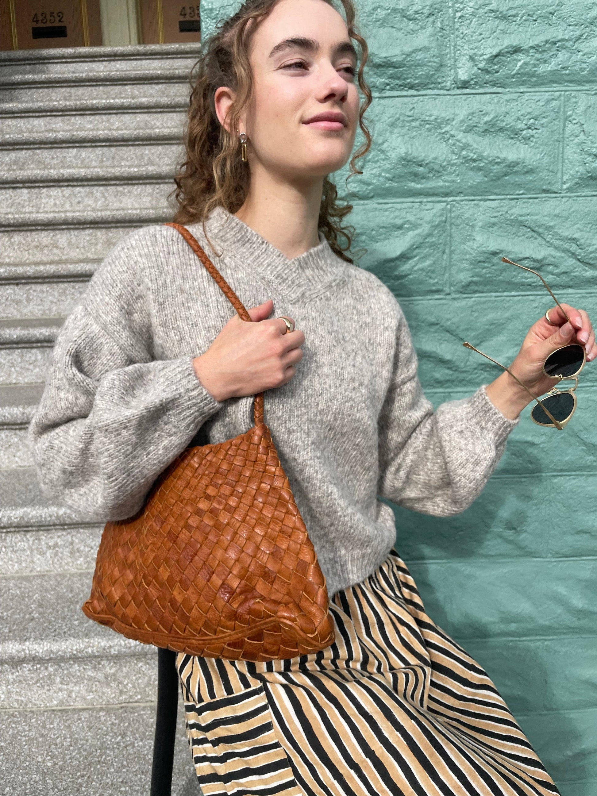 Model styling the Palar Tan Bag over the shoulder with a grey knit and striped trousers