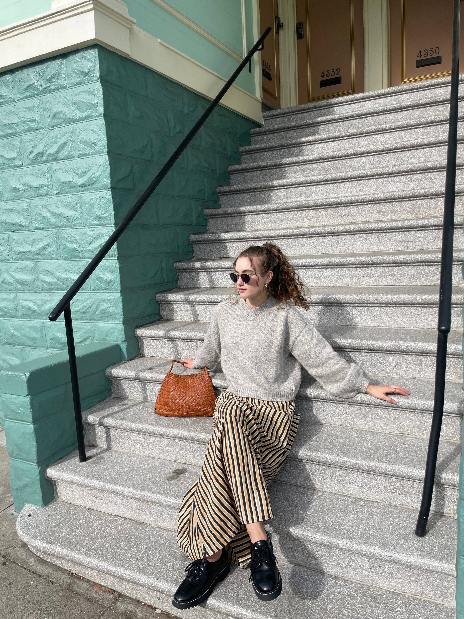 Model seated on outdoor steps with the Palar Tan Bag beside her