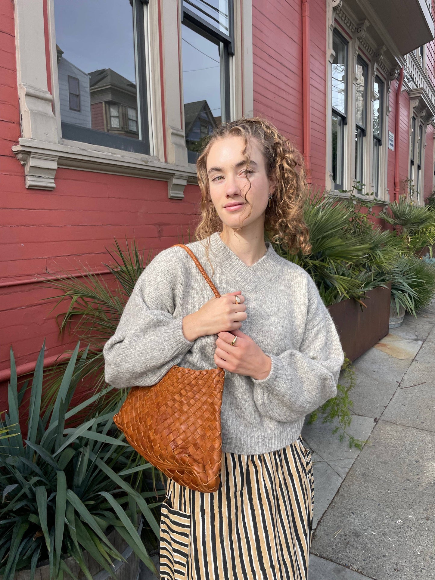 Model wearing the Palar Tan Bag with a grey sweater and striped trousers outdoors