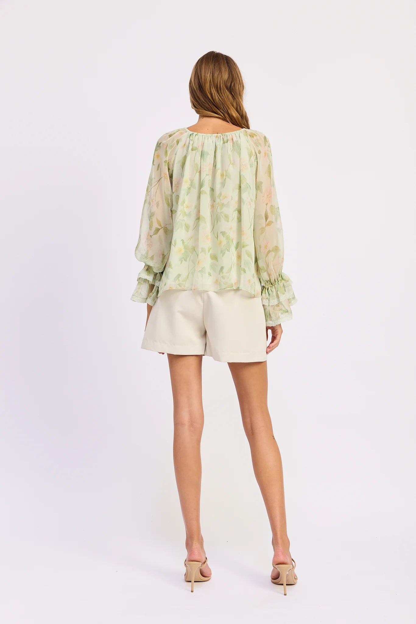 Back view of the Paloma Blouse featuring a relaxed flowing silhouette in a soft sage green floral chiffon with long sleeves and ruffled cuffs.