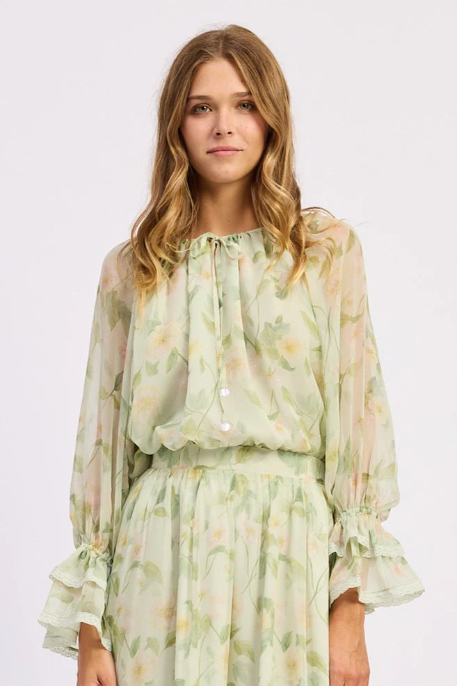 Close-up of the Paloma Blouse showing the gathered tie neckline, delicate floral print, and sheer lightweight fabric with soft ruffled sleeve details.