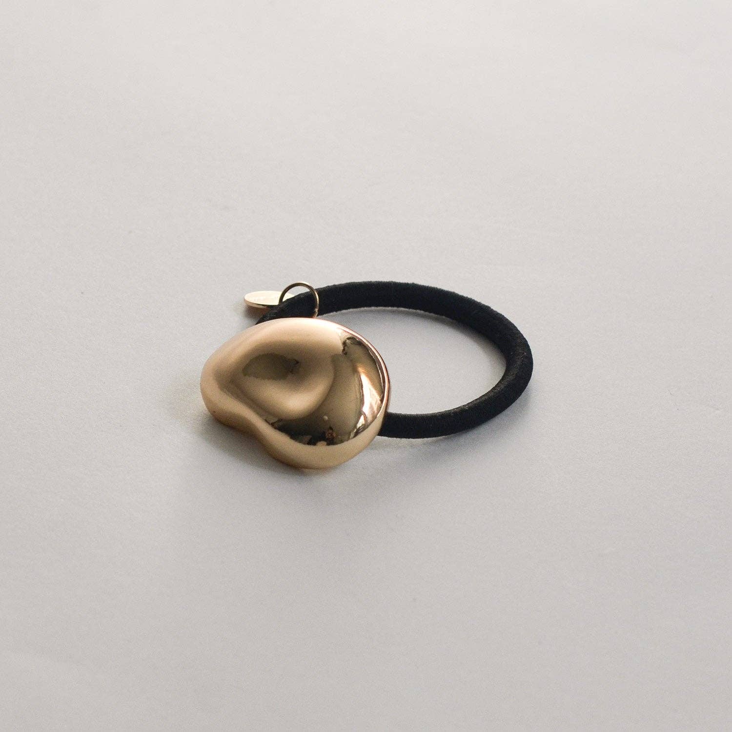 Angled front view of the polished gold pebble-shaped cuff and black hair elastic.