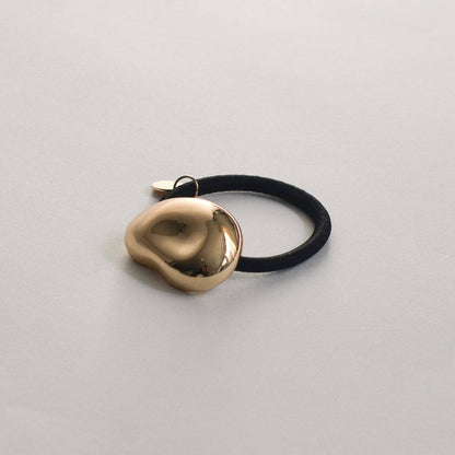 Angled front view of the polished gold pebble-shaped cuff and black hair elastic.