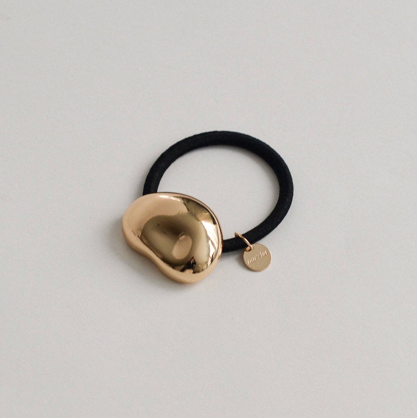 Gold pebble-shaped metal cuff hair tie with black elastic on a light neutral background.