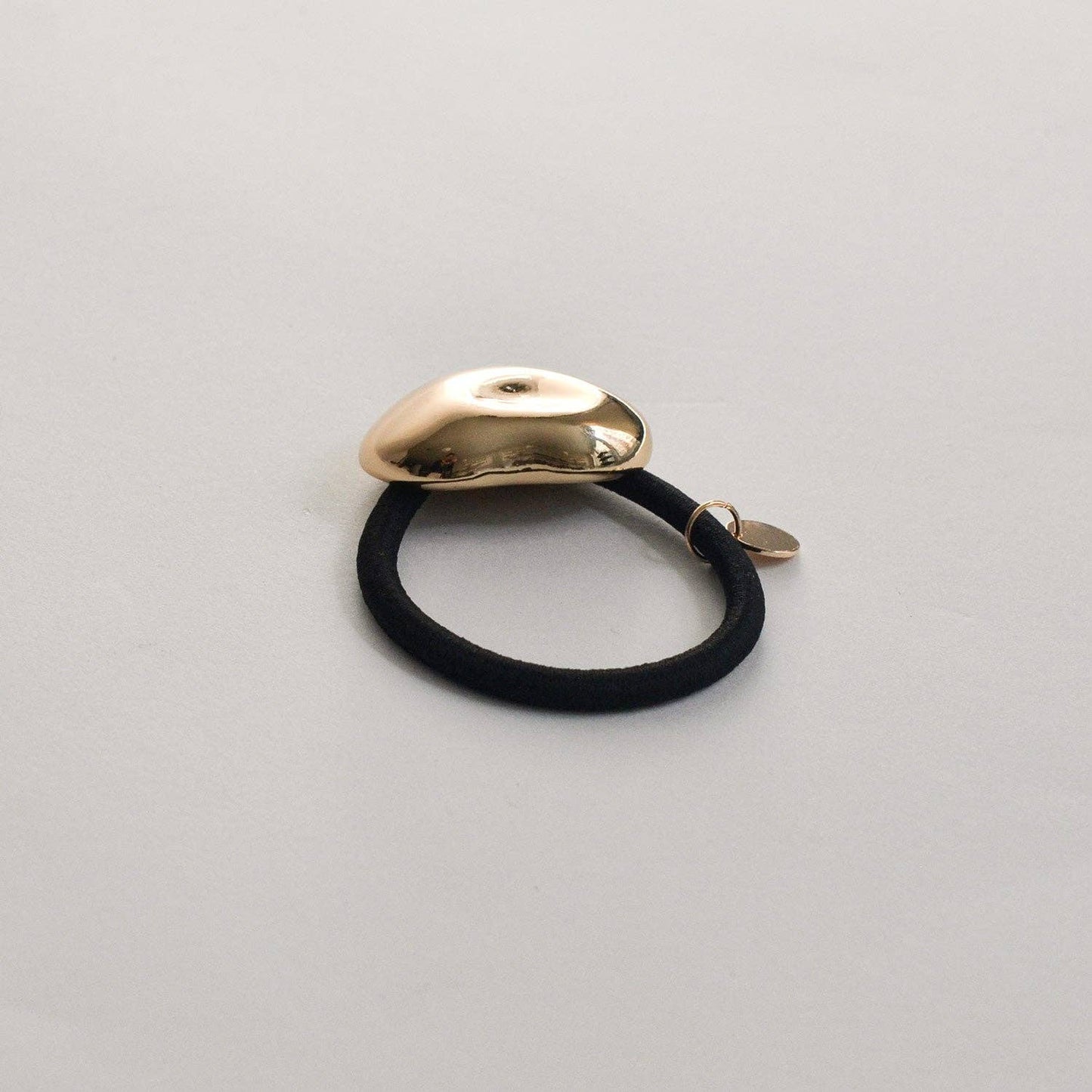 Rear angled view of the gold pebble-shaped cuff and secure black elastic hair tie.