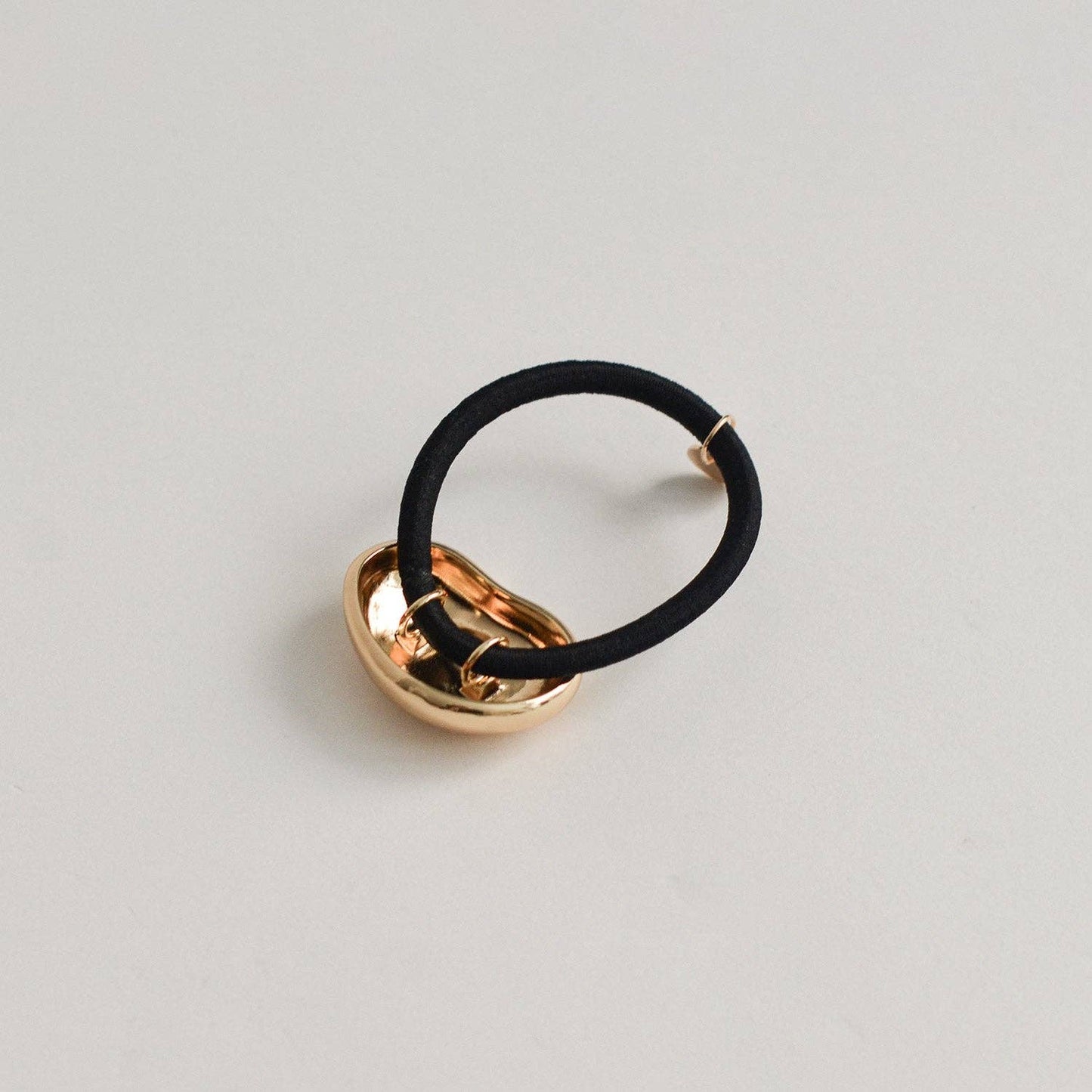 Underside detail of the gold pebble-shaped metal cuff attached to a black hair tie.