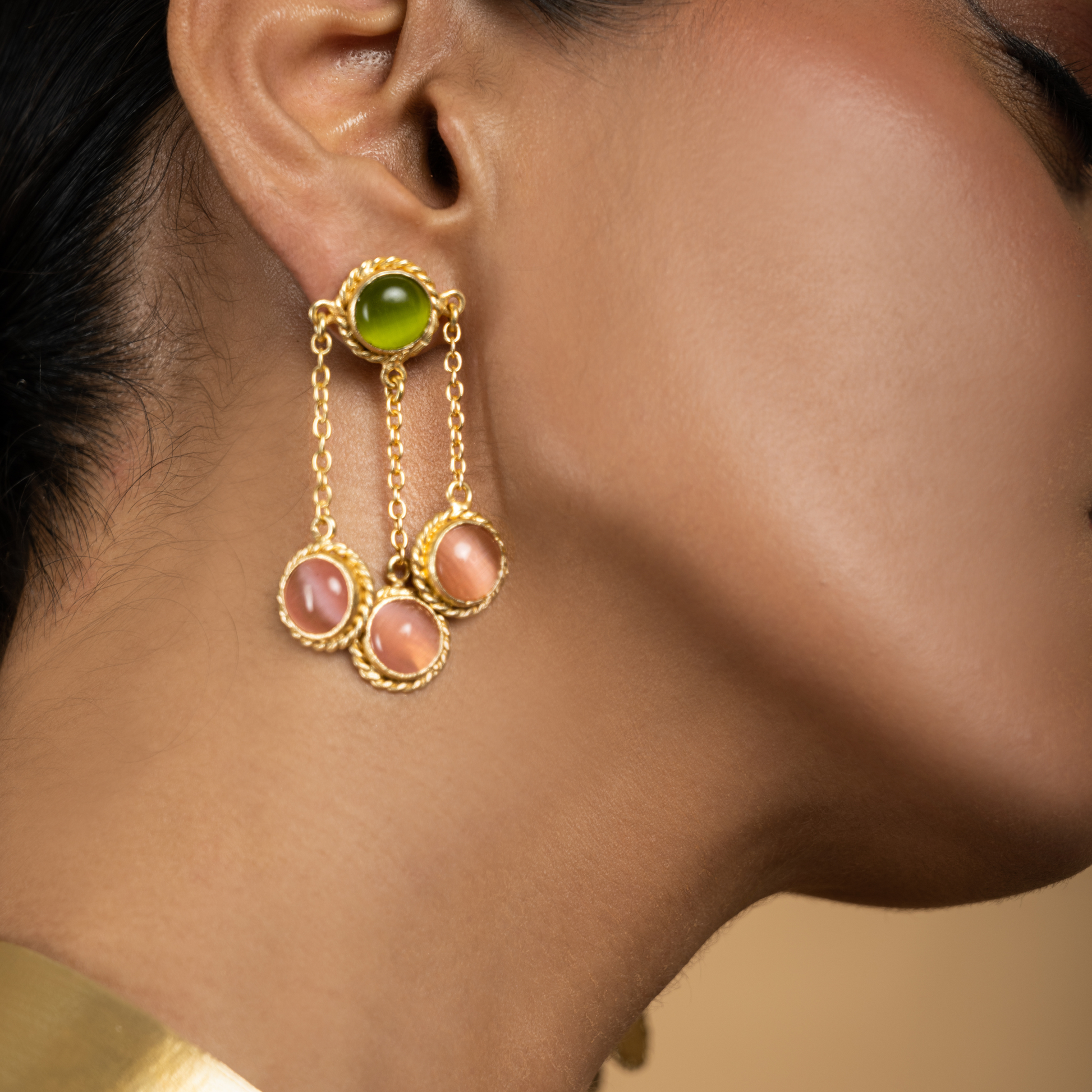 Close-up of matching gold drop earrings featuring green and pink stones worn by a model.