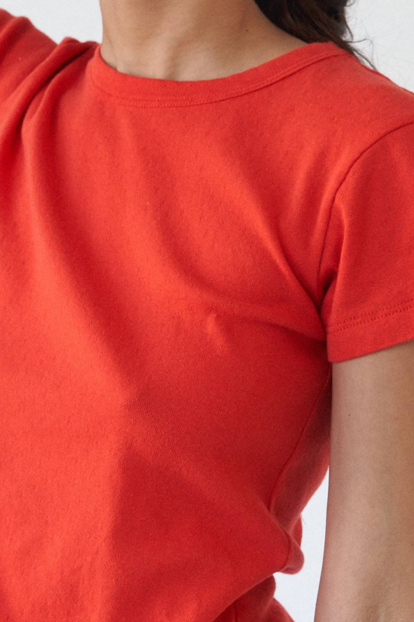 Close-up of the Pointelle Baby Tee in red orange showing the cap sleeve, chunky neck binding, and textured pointelle knit.