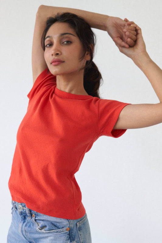 Model wearing the Pointelle Baby Tee in red orange with light wash jeans, shown from the front with arms raised.