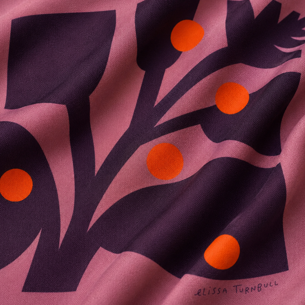 Close-up of a silk scarf with deep purple botanical shapes, mauve wavy forms, and orange-red dots.