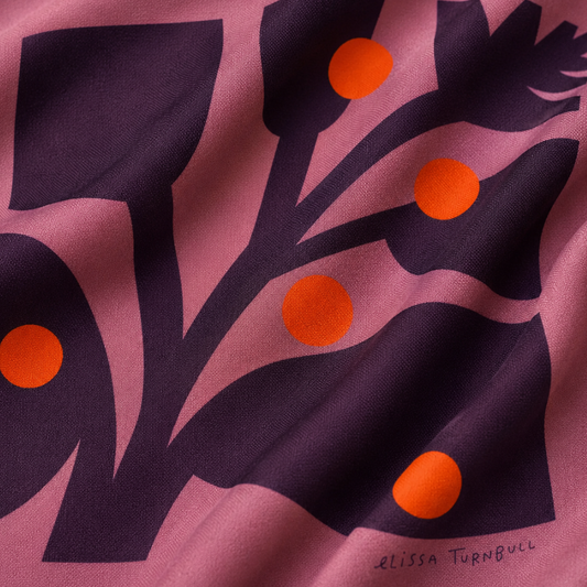 Close-up of a silk scarf with deep purple botanical shapes, mauve wavy forms, and orange-red dots.