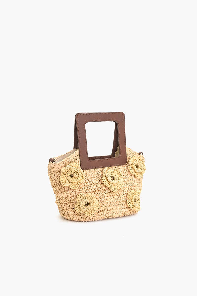 Front view of a small woven beige raffia tote with flower details and a square brown top handle.