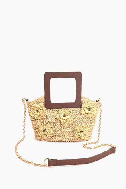 Woven beige raffia top-handle tote with raffia flower accents, square brown handle, and long chain strap.