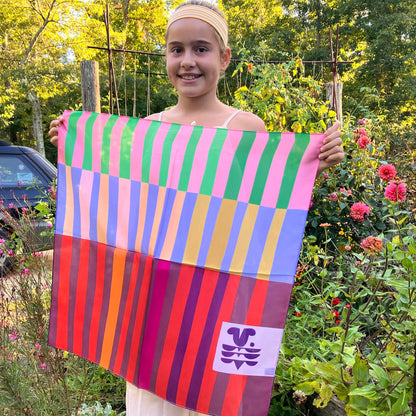 Model holding the Red Colorblock silk scarf outdoors in a garden, showing the full striped bandana design.