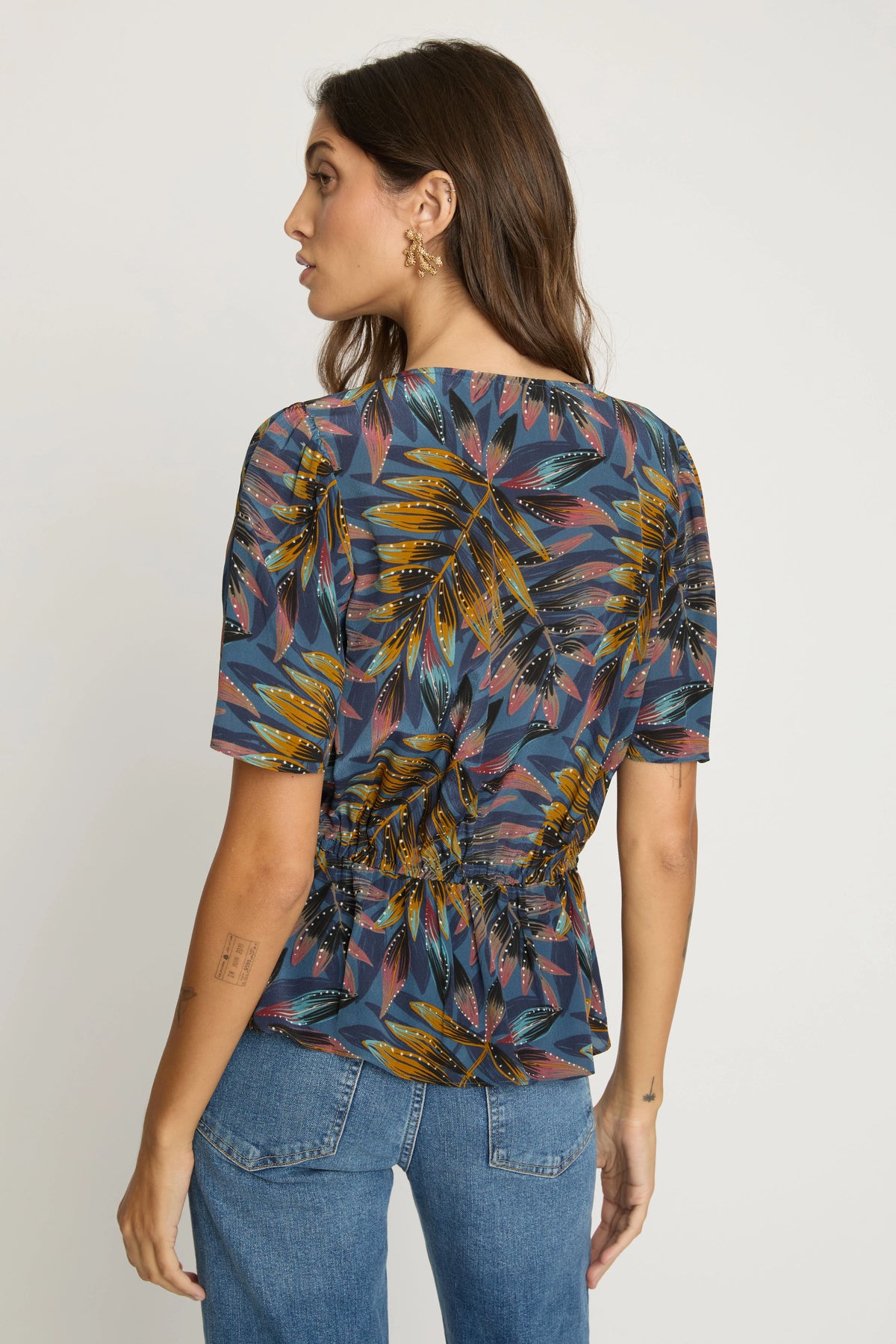 Back view of the Rhea Top showing the short sleeves, gathered elasticized waist, and subtle peplum silhouette.