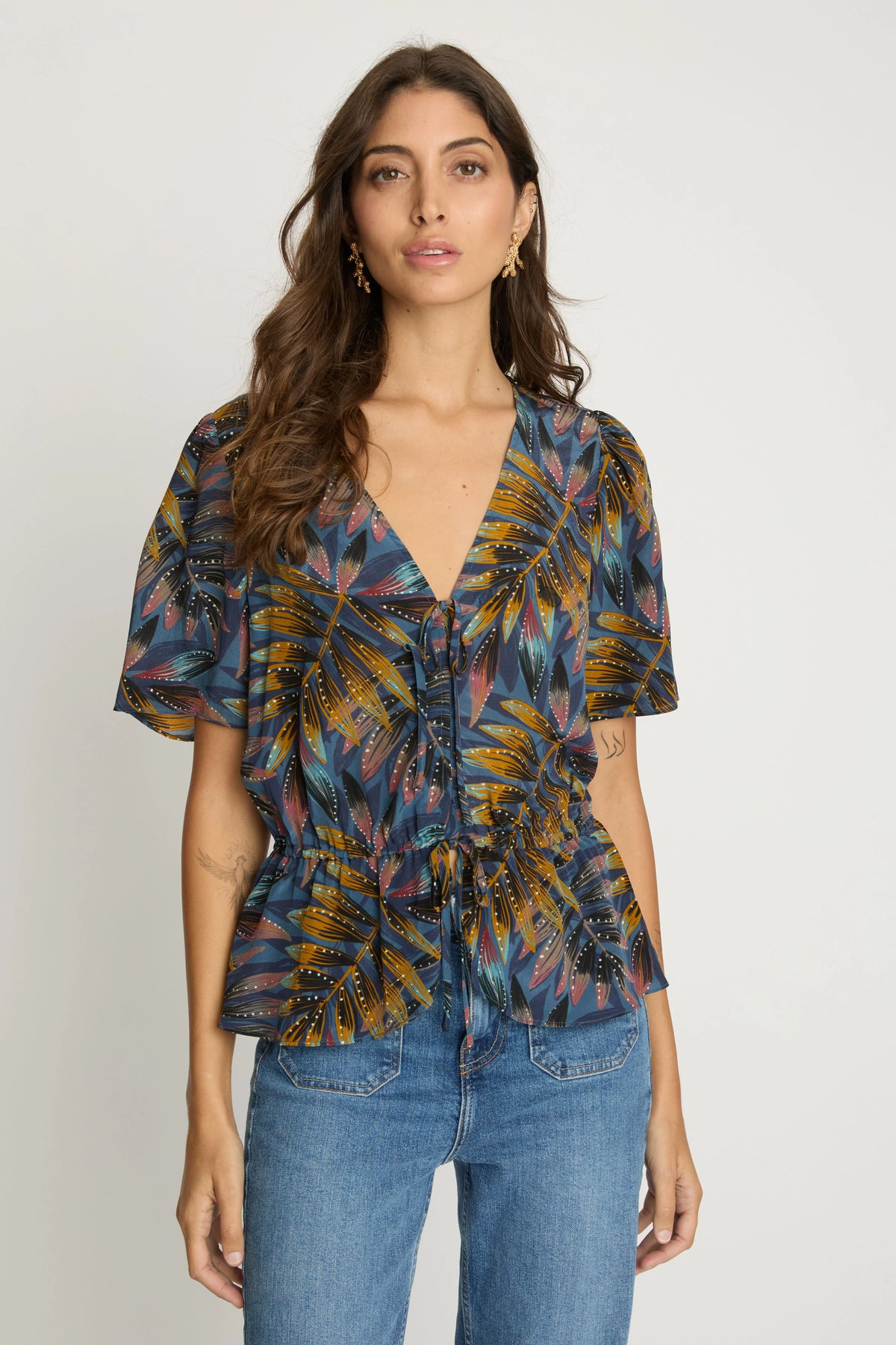 Front view of the Rhea Top featuring a V-neckline, tie-front detail, flutter sleeves, and an elasticized waist.