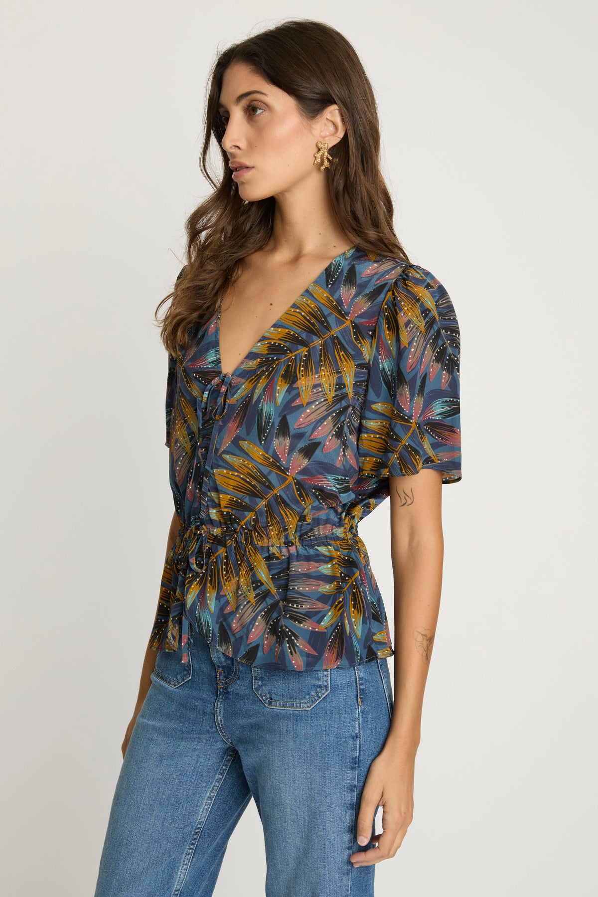 Three-quarter view of the Rhea Top showing its painterly palm print, softly gathered bodice, and peplum hem.