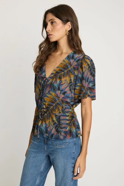 Three-quarter view of the Rhea Top showing its painterly palm print, softly gathered bodice, and peplum hem.