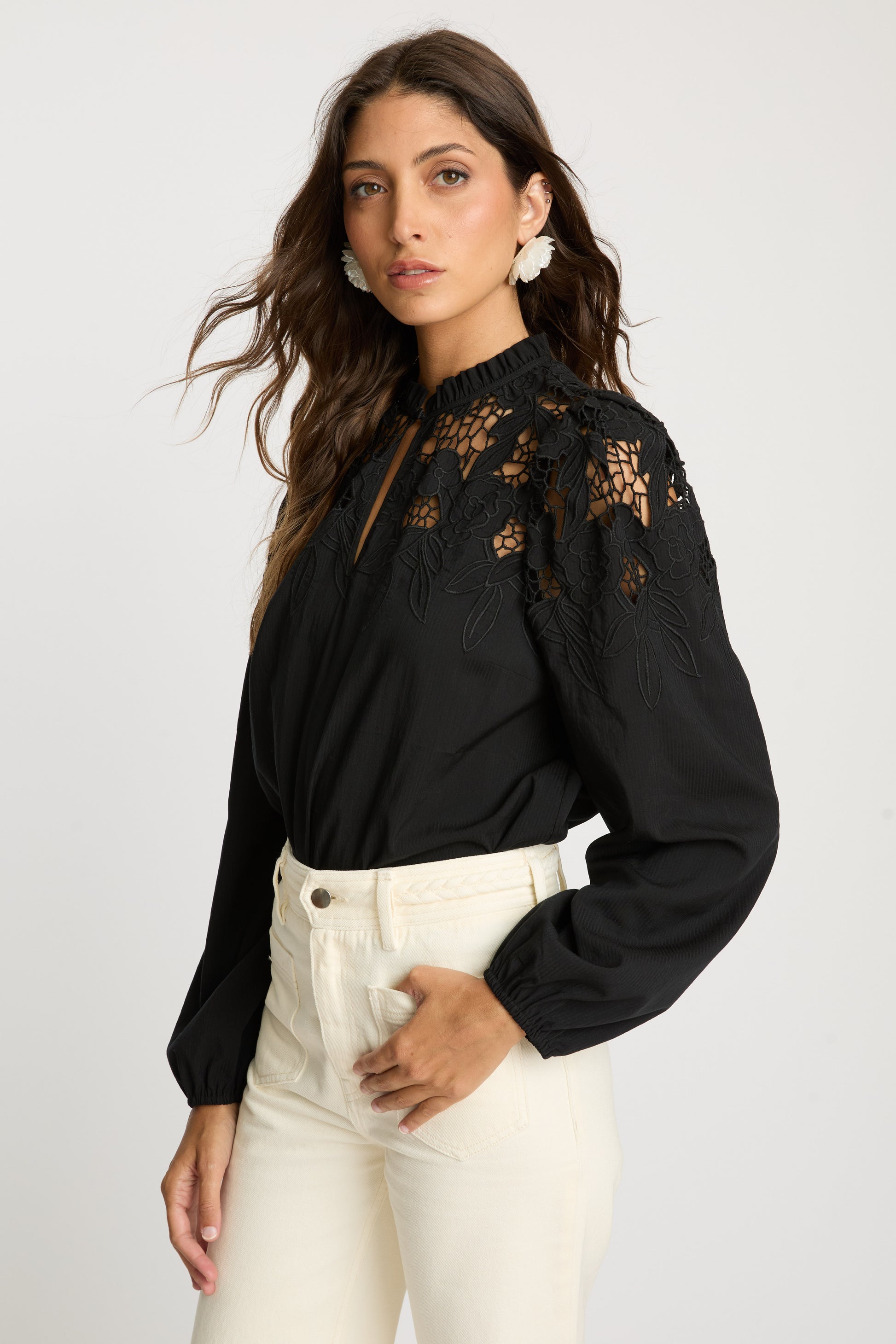 Angled portrait view of the Riana Reversible Top in black showcasing floral lace detailing across the shoulders, sheer embroidered panels, and gathered long sleeves.