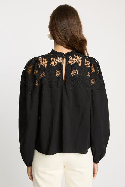 Rear detail view of the Riana Reversible Top in black showcasing semi-sheer floral lace panels, embroidered shoulder detailing, keyhole back closure, and long sleeves with gathered cuffs.