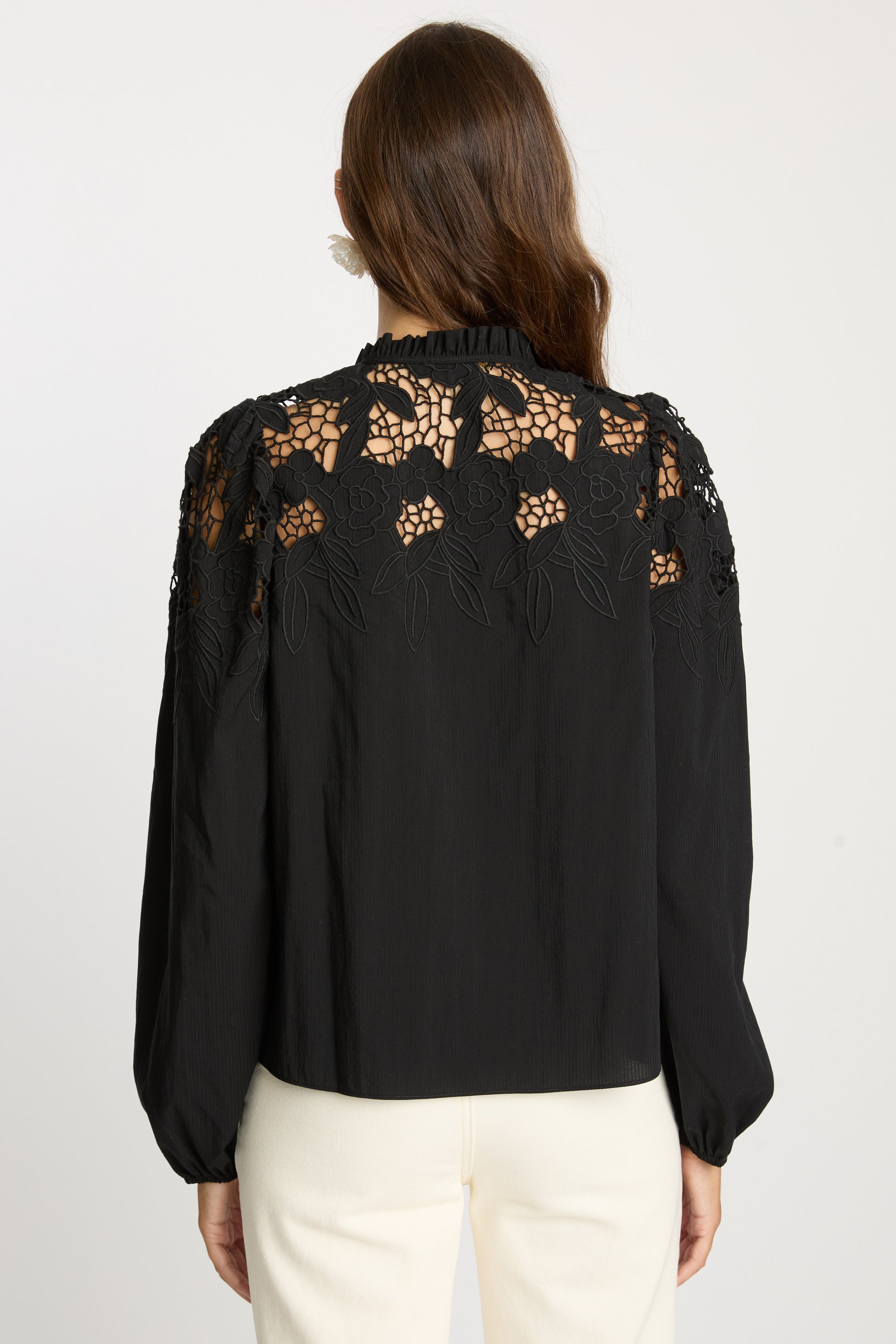 Back view of the Riana Reversible Top in black featuring intricate floral lace embroidery across the shoulders and upper back, a high ruffled neckline, and long gathered sleeves.