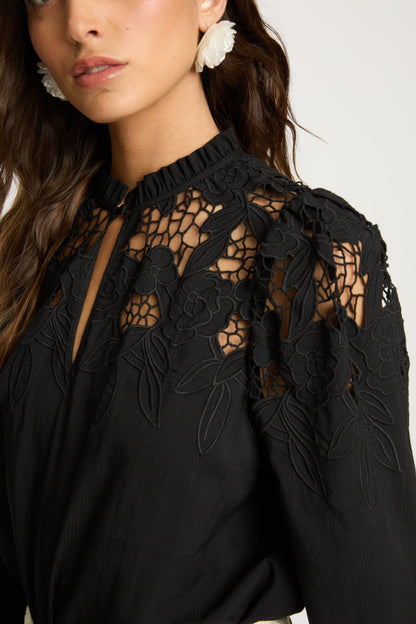 Close-up of the Riana Reversible Top in black highlighting the intricate floral lace embroidery, sheer mesh detailing, and ruffled neckline at the shoulder and upper bodice.