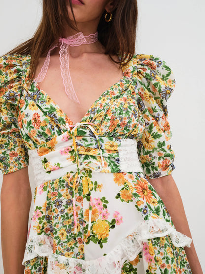 Detail view of the Rosalyn Mixed Floral Print Mini Dress highlighting the floral print, lace trim, shirred waist panels, front tie, and puff sleeve design.