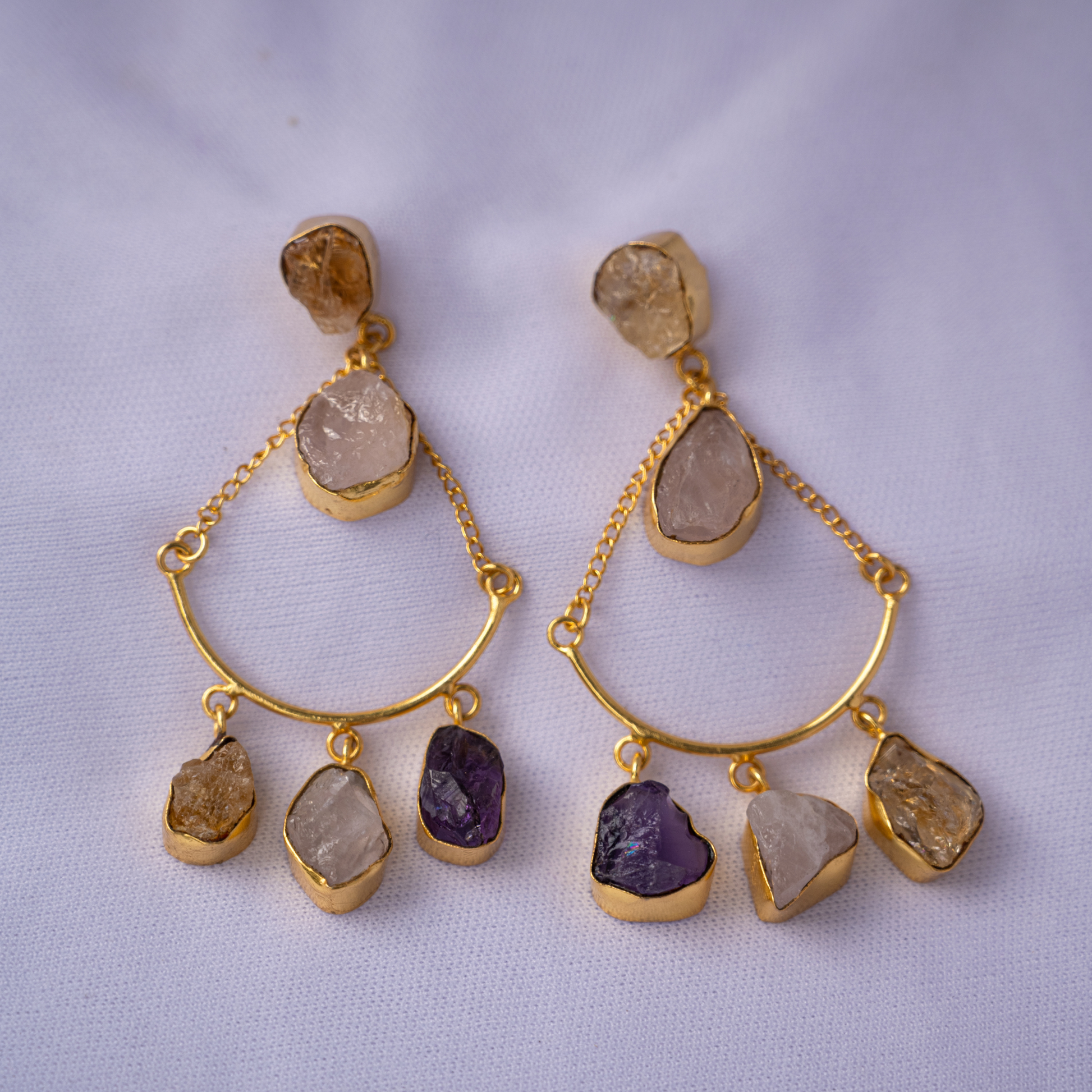 Pair of gold-plated dangle earrings featuring natural rose quartz, citrine, and amethyst stones on a soft lavender background.