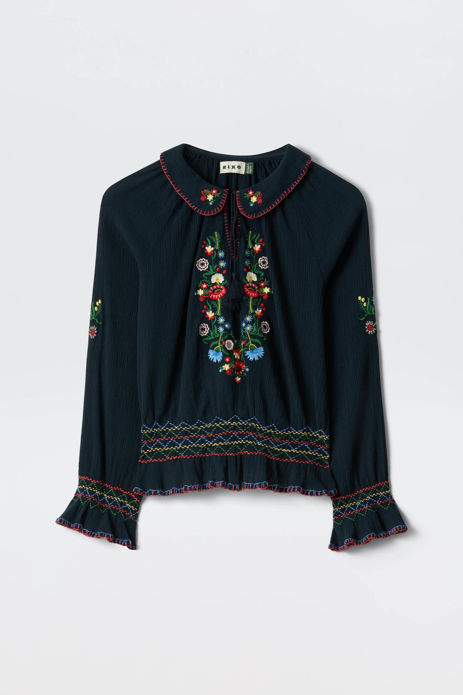 Flat lay of the navy Sofira Top with colorful floral embroidery, tie-neck detail, and ruffled cuffs