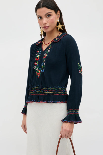Model wearing the Sofira Top in navy viscose georgette with colorful floral embroidery and ruffled trim