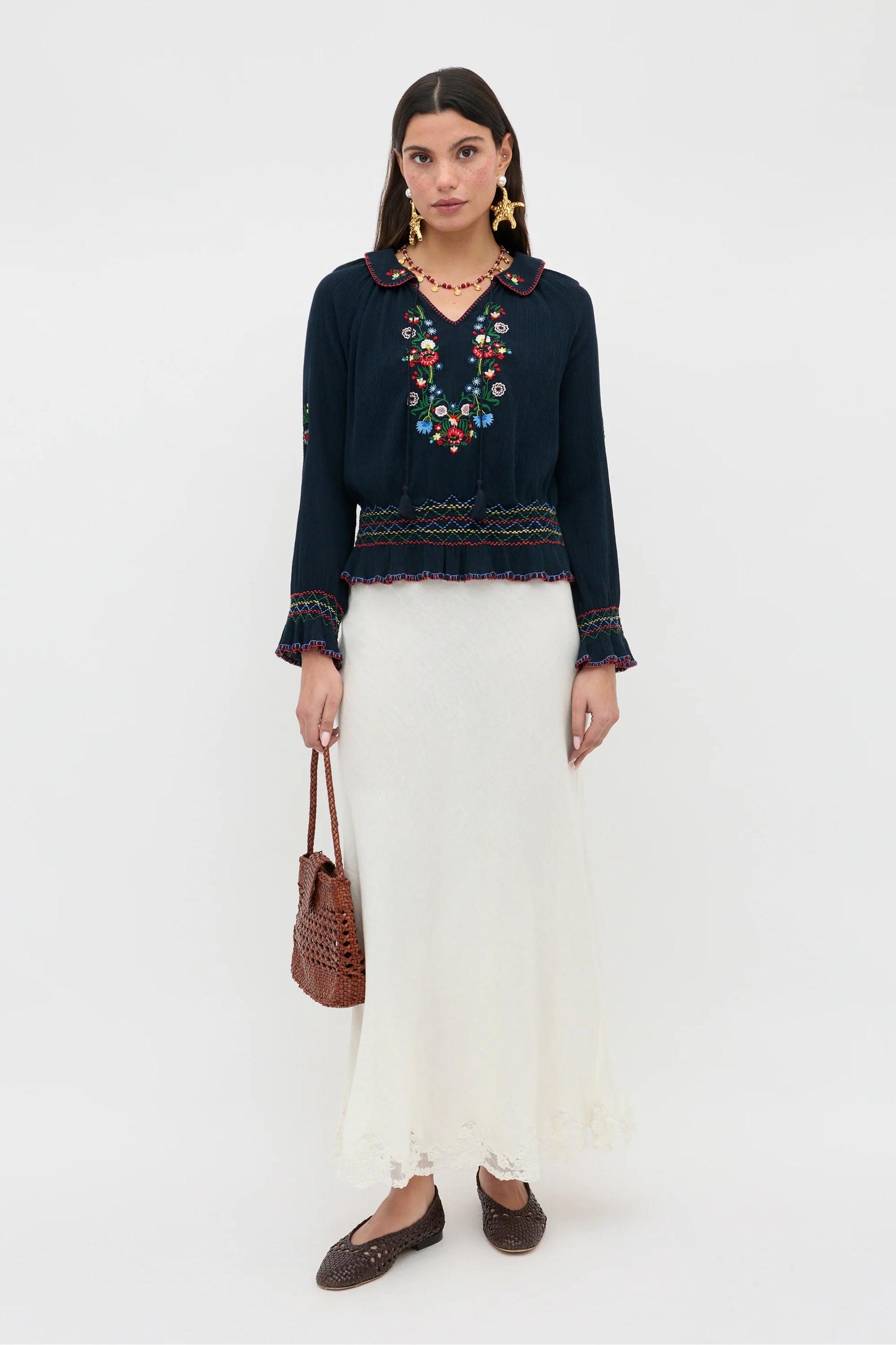 Full-length view of the Sofira Top styled with a cream skirt, featuring embroidered floral details and relaxed long sleeves
