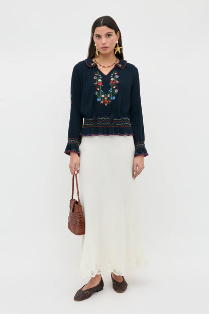 Full-length view of the Sofira Top styled with a cream skirt, featuring embroidered floral details and relaxed long sleeves