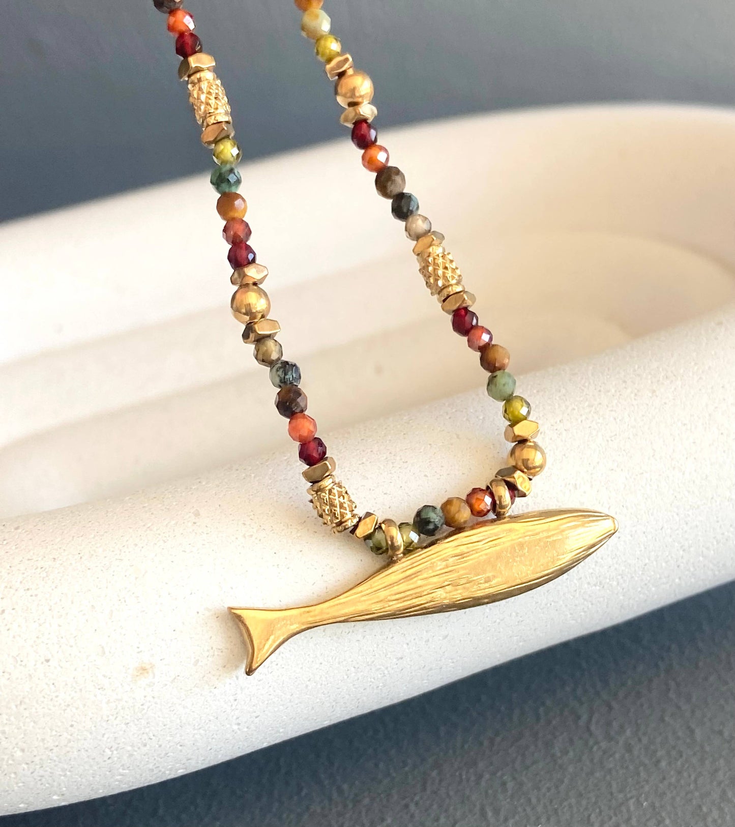 Close-up of the Somy Necklace with multicolored gemstone beads and a gold fish-shaped pendant.