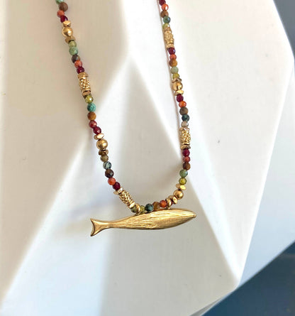 Somy Necklace displayed on a white stand with multicolored gemstone beads and a gold fish-shaped pendant.