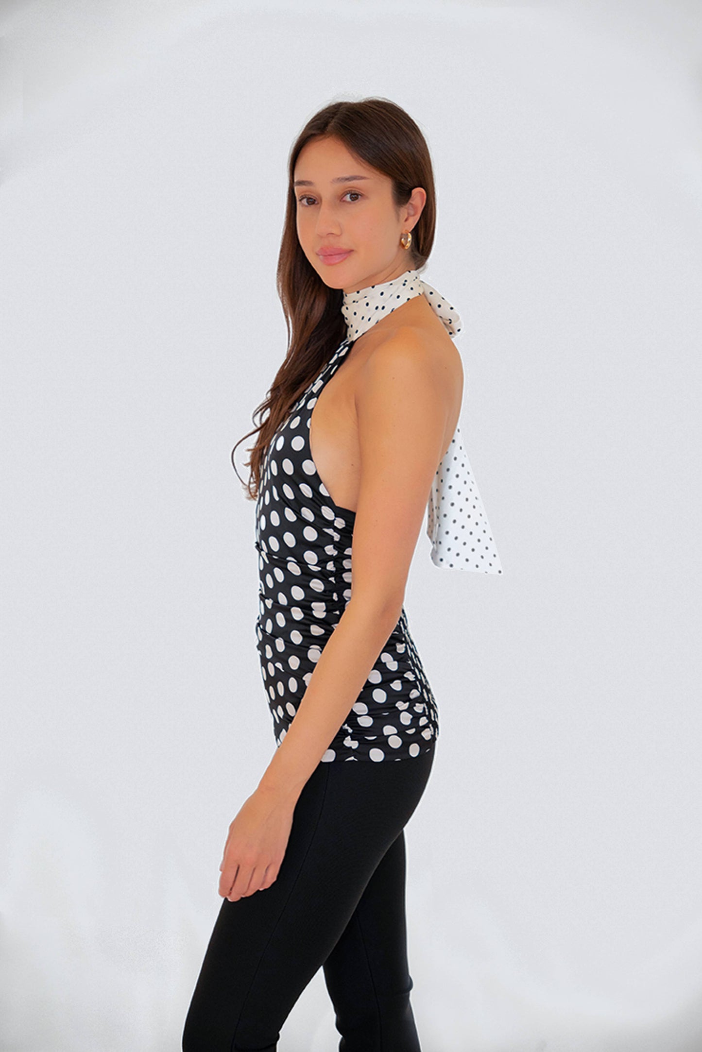 Model wearing the Sophie Contrast Mono Polka Dot Scarf Neck Top in a side profile pose highlighting the halter neckline and satin polka dot finish.