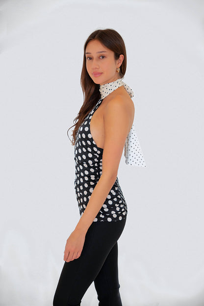 Model wearing the Sophie Contrast Mono Polka Dot Scarf Neck Top in a side profile pose highlighting the halter neckline and satin polka dot finish.
