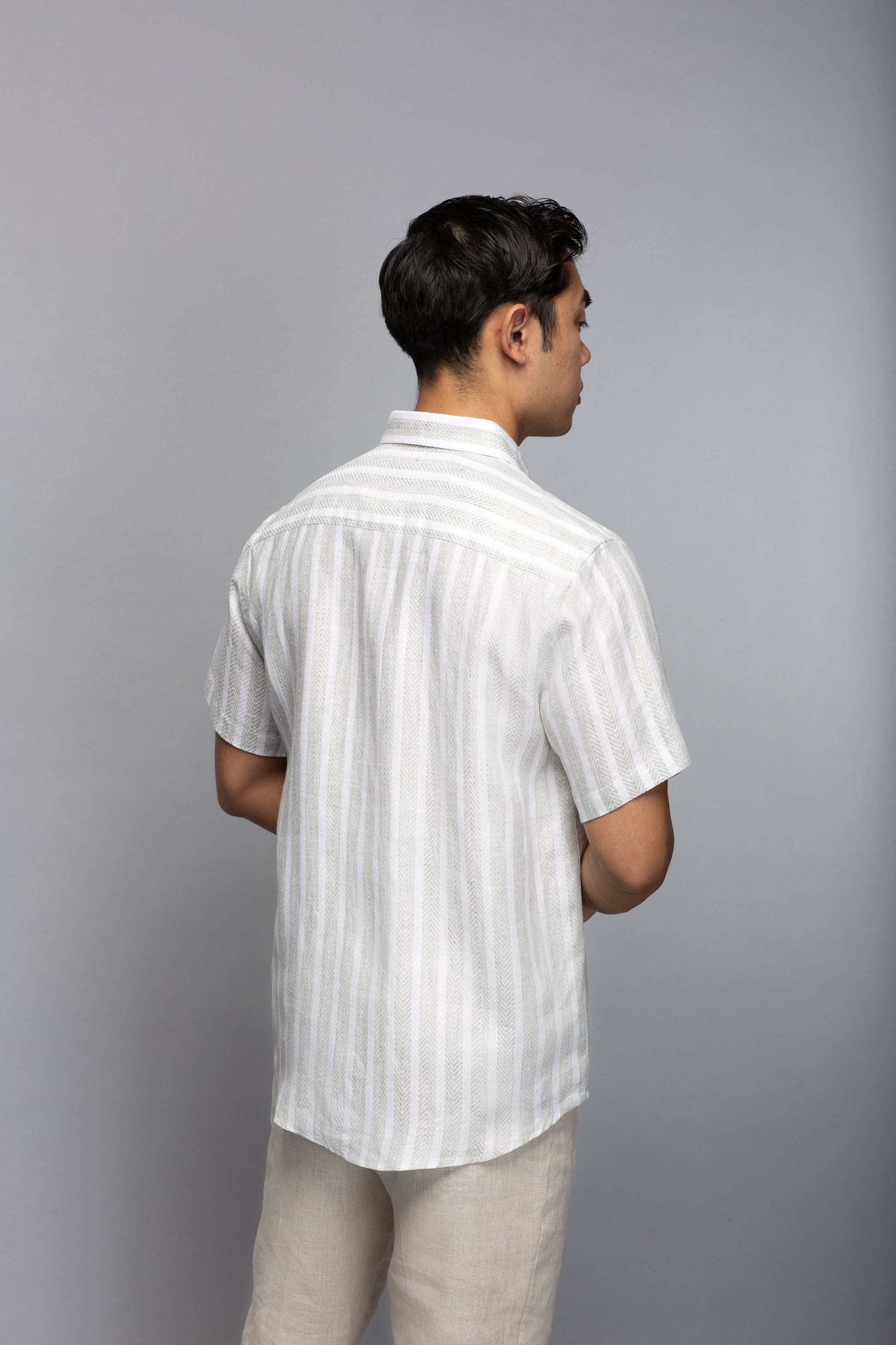 Back view of a model wearing the short-sleeve striped linen shirt with light neutral trousers.