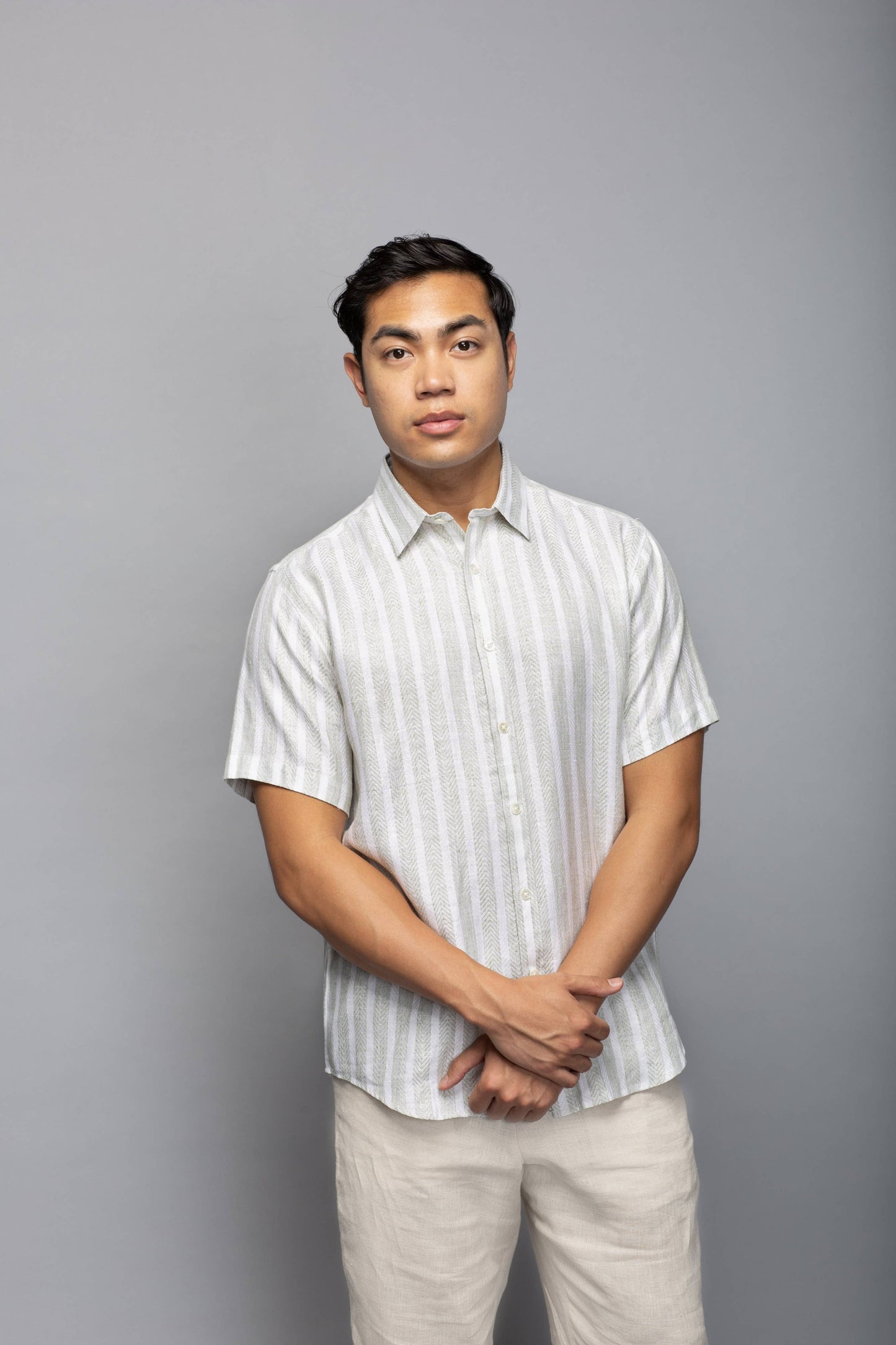 Model wearing the striped short-sleeve linen shirt with light neutral trousers, shown from the front.