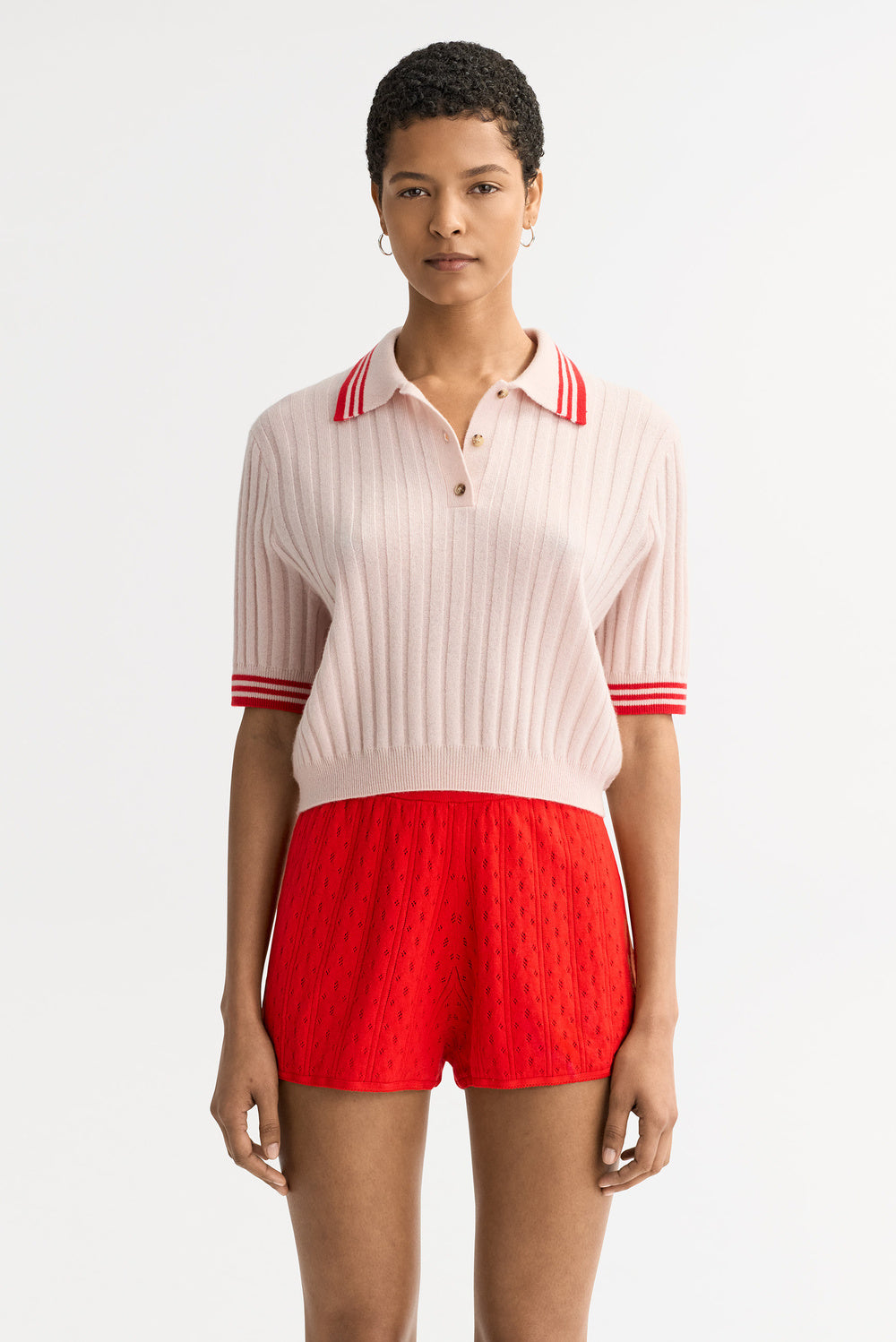 Model wearing the Striped Pique cashmere polo in blush pink with red and white striped collar and cuff accents and ribbed knit texture.
