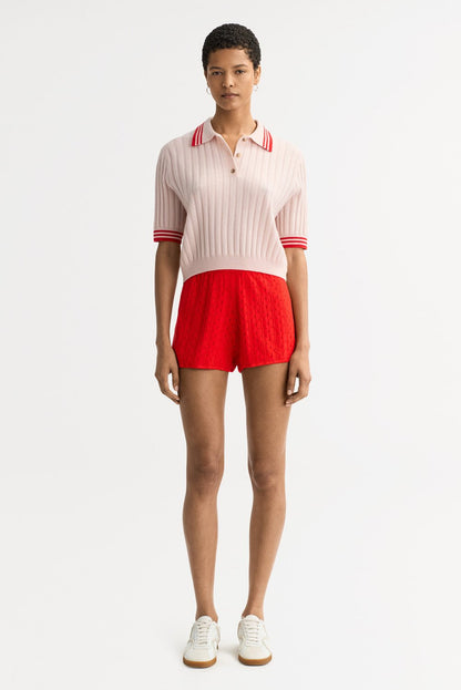 Full-length front view of the blush pink Striped Pique cashmere polo styled with bright red knit shorts and white sneakers.
