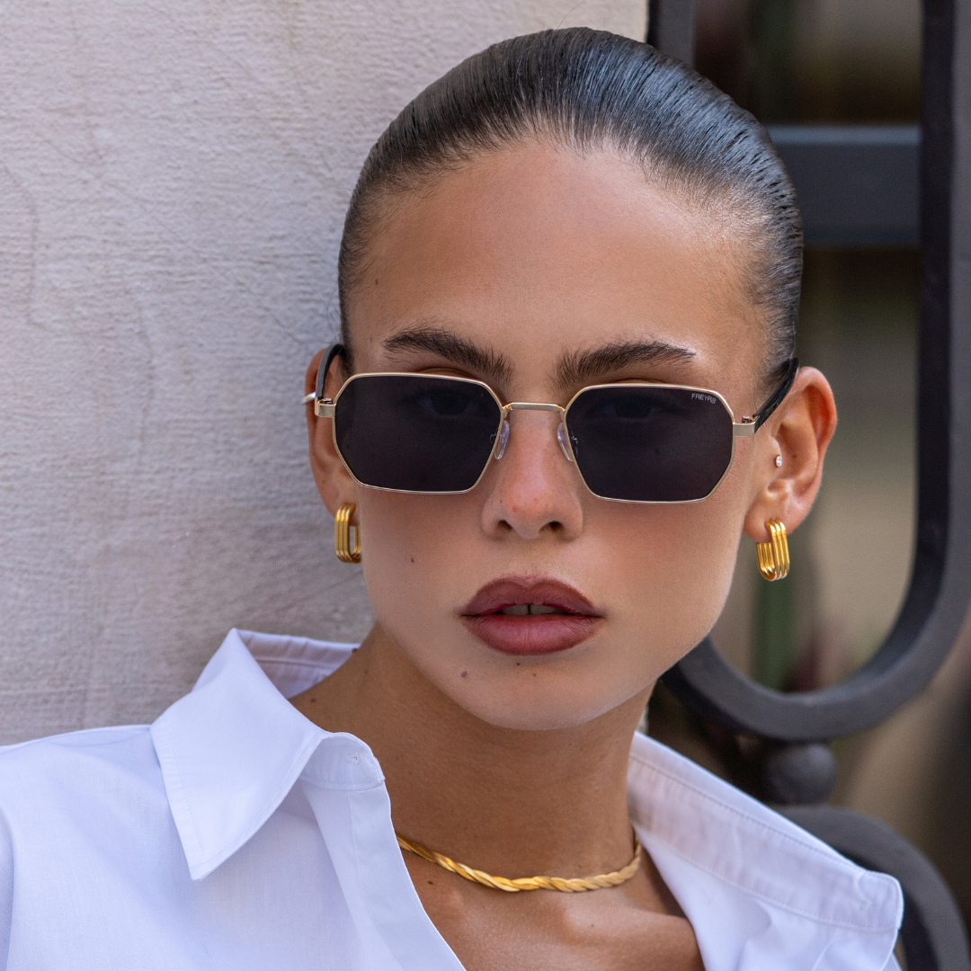 Model wearing Superior unisex sunglasses with a gold frame, gray lenses, and a sleek rectangular shape.
