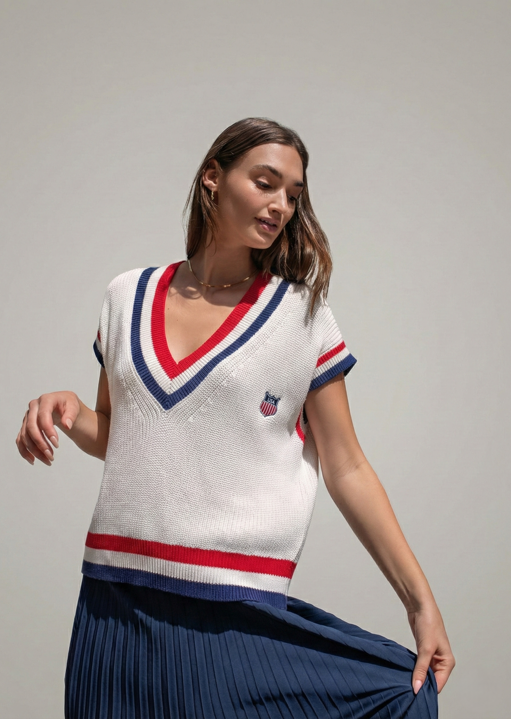 Model wearing the off-white American Shield sweater vest with a navy pleated skirt.