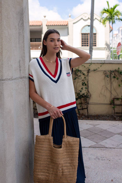 Model styling the American Shield sweater vest with a navy skirt and woven tote bag.