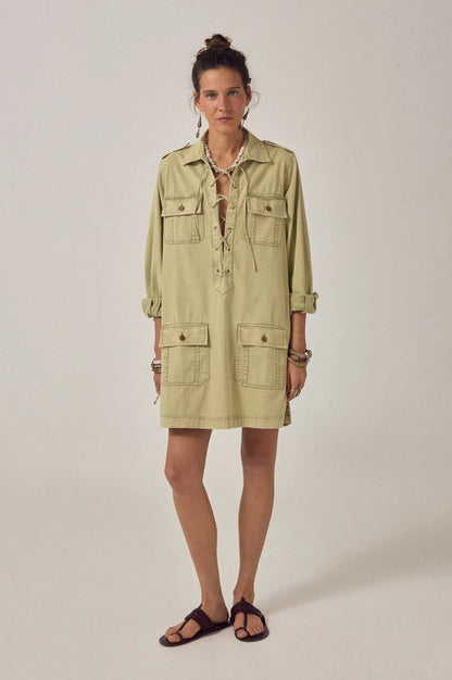 Model wearing the Thalassa Short Dress in Army Khaki featuring a lace-up V-neckline, long sleeves with epaulets, and four flap pockets.
