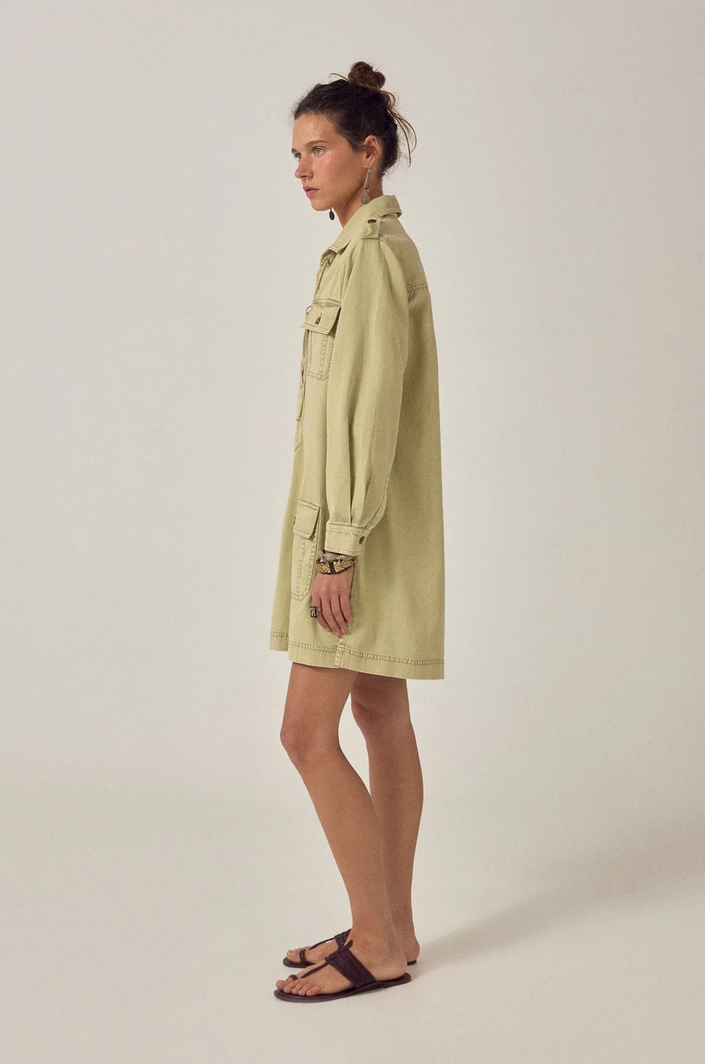 Side profile of the Thalassa Short Dress in Army Khaki featuring a relaxed fit, long sleeves, and structured utility-inspired silhouette.