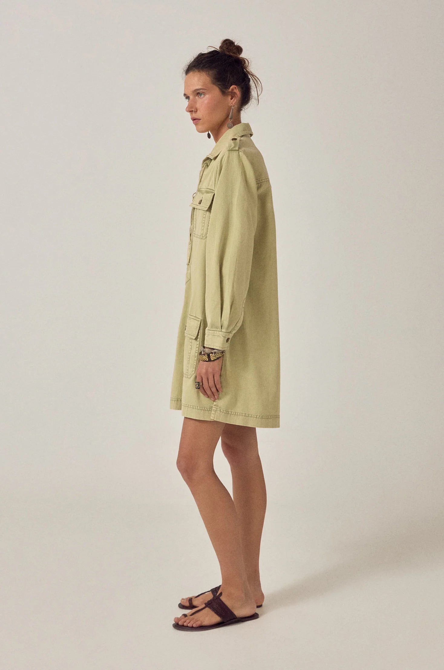 Side profile of the Thalassa Short Dress in Army Khaki featuring a relaxed fit, long sleeves, and structured utility-inspired silhouette.