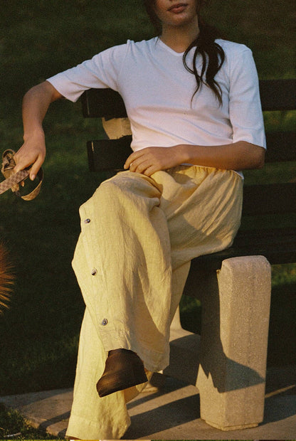 Model seated outdoors wearing Tilda Linen Pant in Sunflower styled with a white fitted tee